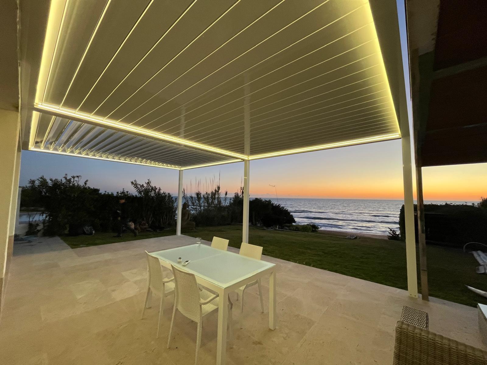 Interior de pérgola bioclimática con vistas al mar al atardecer