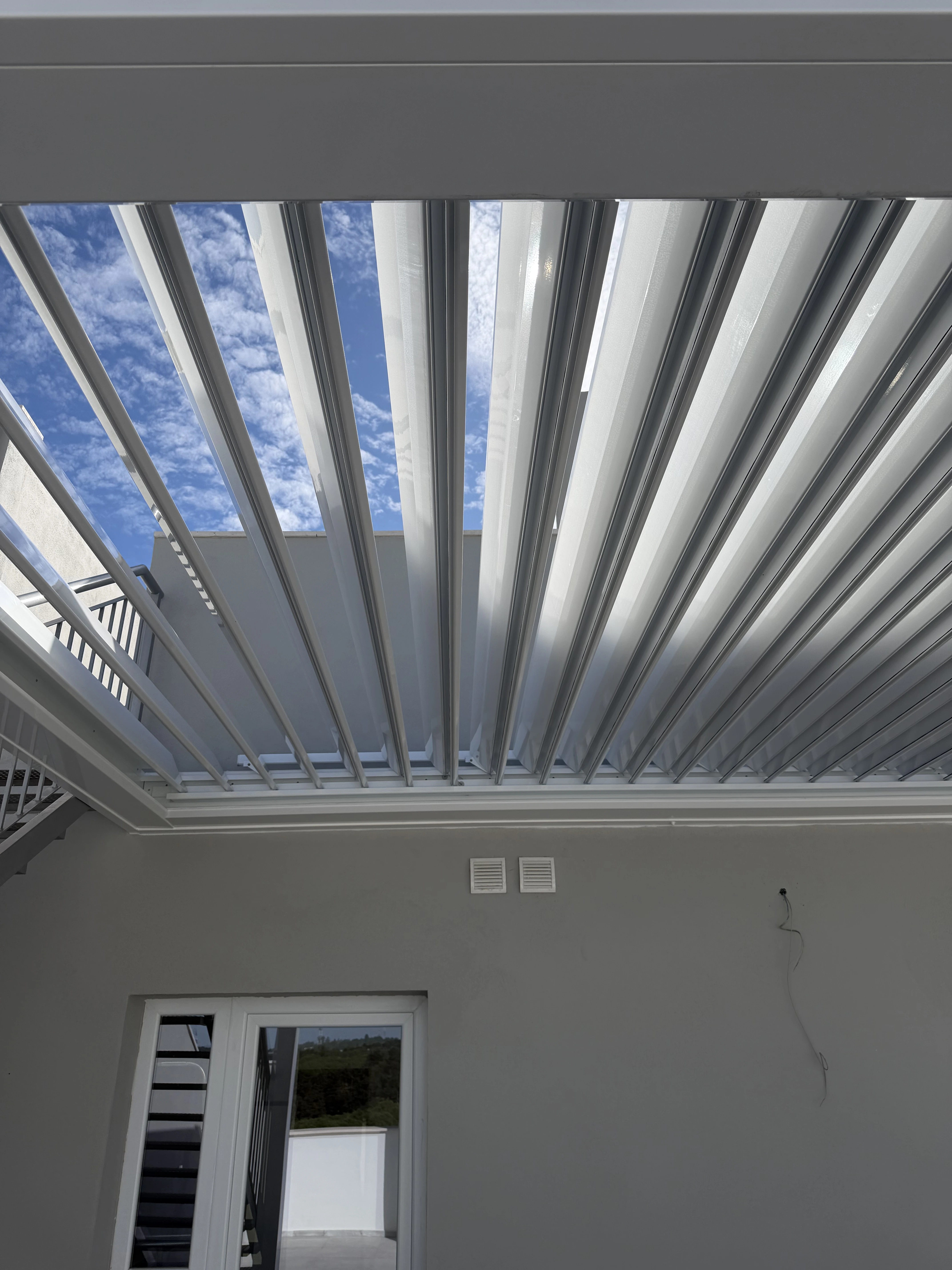 Lamas orientables de una pérgola bioclimática en posición abierta, permitiendo el paso de luz