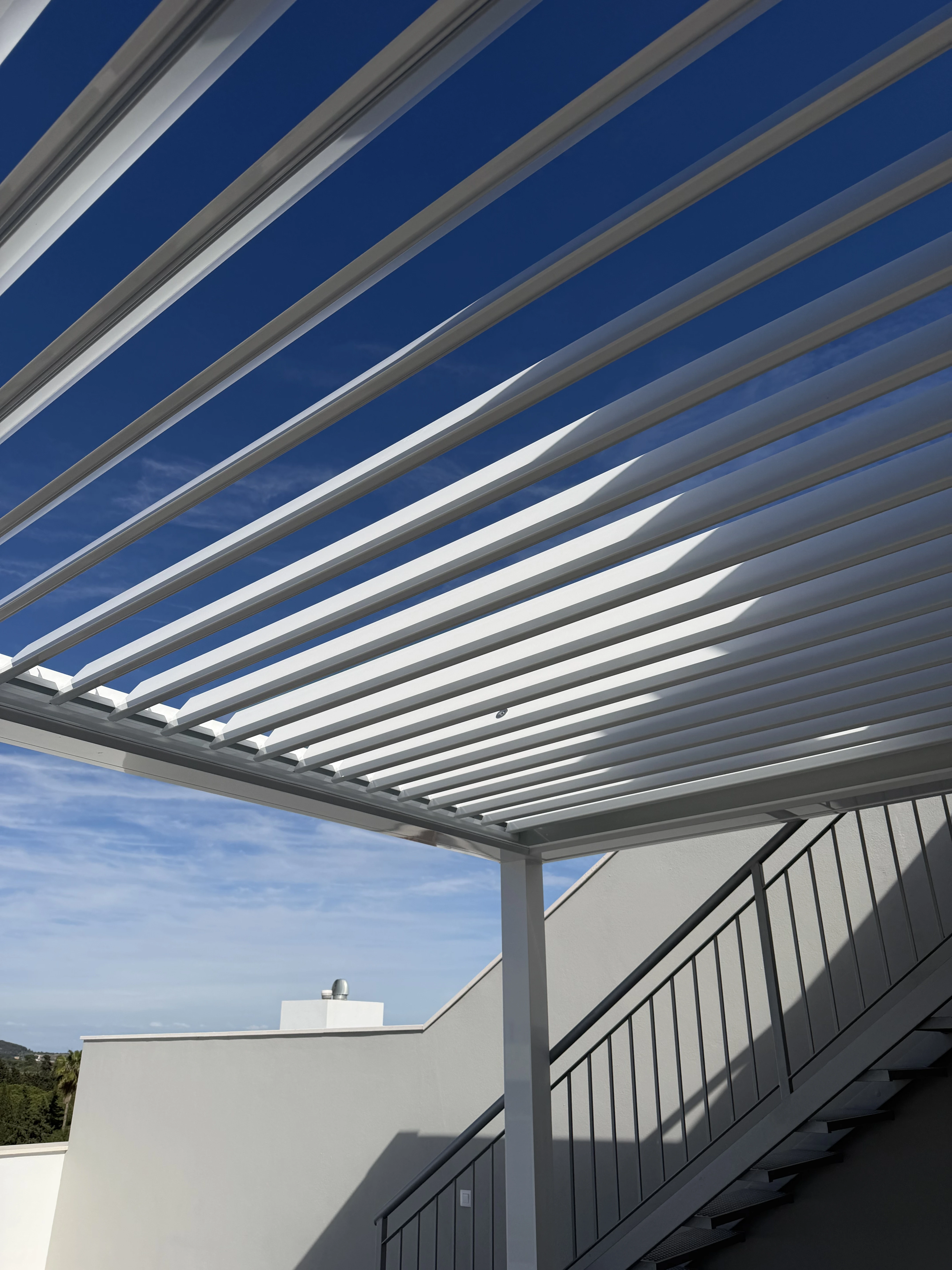 Pérgola bioclimática blanca con lamas orientables en azotea, vista contrapicada