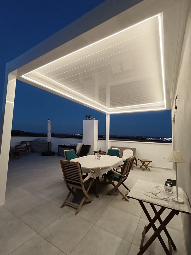Comedor exterior bajo la pérgola con la iluminación perimetral encendida